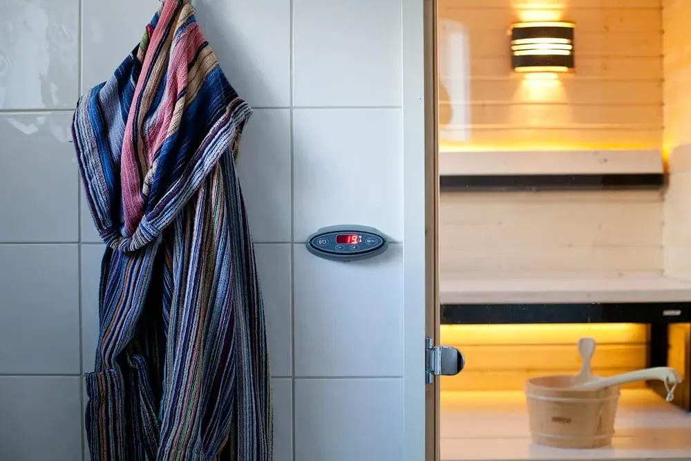 Bathrobe beside a sauna control panel and a glass sauna door