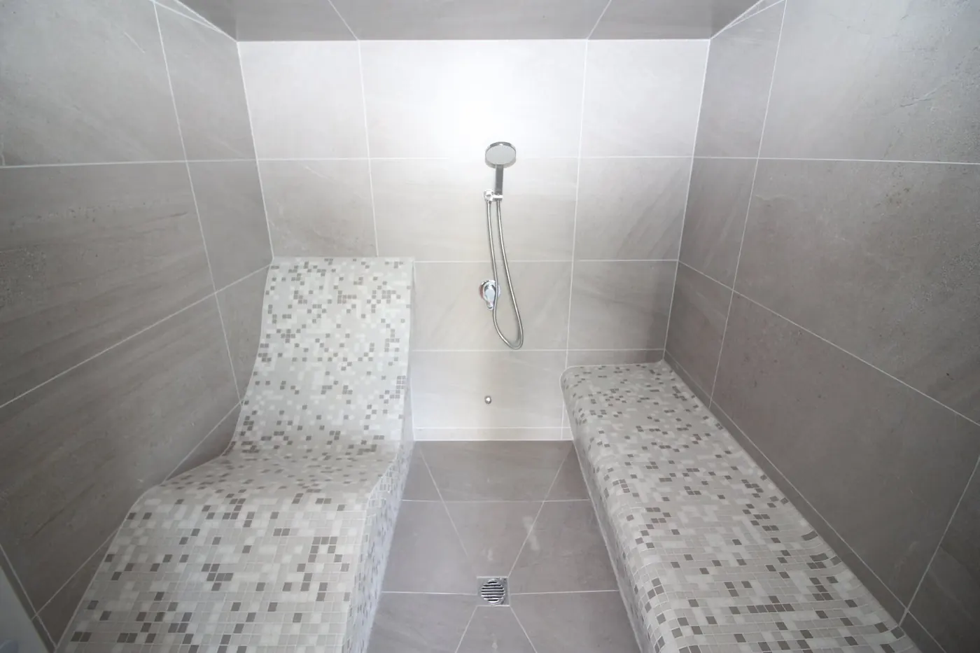 Tiled steam room with mosaic benches and a hand shower